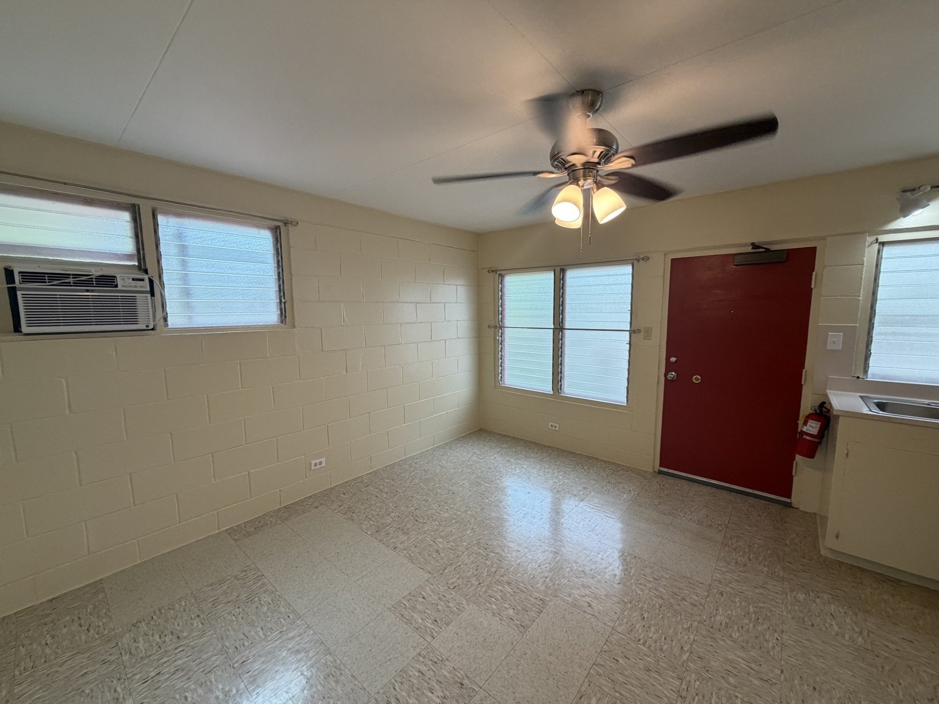 A room with a ceiling fan and a red door.